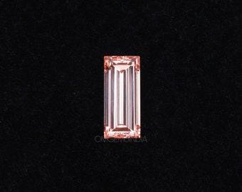 May include: A rectangular, peach-colored gemstone with a baguette cut, set against a black background. The gem features parallel, linear facets that reflect light, creating a shimmering effect. The stone's color is a soft, warm hue.