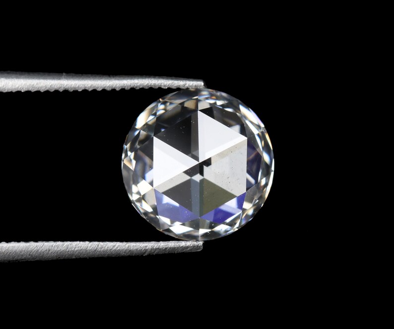 May include: A clear, round-cut diamond held by silver tweezers against a black background. The diamond's facets reflect light, creating a brilliant display of white and blue hues. The gem is a focal point, showcasing its clarity and cut.