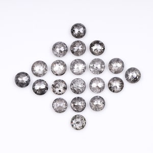 Puede incluir: Una colección de 16 diamantes negros redondos y facetados dispuestos en forma de diamante sobre un fondo blanco.