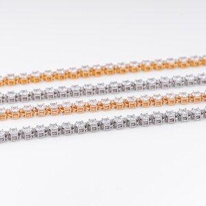K&ouml;nnte beinhalten: Vier Diamant-Tennisarmb&auml;nder in Gold- und Silbert&ouml;nen werden vor einem wei&szlig;en Hintergrund gezeigt. Die Armb&auml;nder bestehen aus quadratisch geschliffenen Edelsteinen, die in einer durchgehenden Linie angeordnet sind und einen funkelnden und eleganten Look erzeugen.