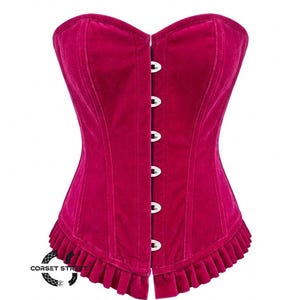 May include: A magenta velvet corset with a ruffled hem and a row of silver-colored clasps down the front. The corset has a structured design and a sweetheart neckline. The text "CORSET STREET" is visible on the bottom left.