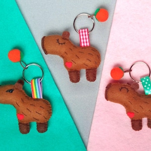 May include: Three felt capybara keychains with orange fruit charms. Each keychain has a different colored ribbon.
