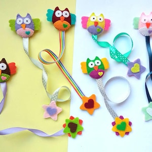 Op de afbeelding: Set van acht vilt uil boekenleggers met kleurrijke linten en ster- en hartversieringen. Elke uil heeft een andere kleur en patroon.