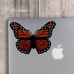 May include: A black and orange butterfly sticker with glitter accents on a silver laptop.