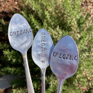 Pode incluir: Tr&ecirc;s colheres de prata com a palavra "OREGANO" gravada. As colheres s&atilde;o usadas como marcadores de jardim.