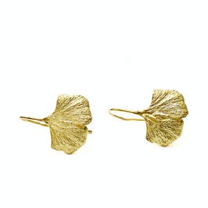 Op de afbeelding: Een paar goudkleurige oorbellen, elk in de vorm van een ginkgoblader. De oorbellen hebben een getextureerd oppervlak en een haaksluiting. De bladeren zijn gedetailleerd met aderachtige patronen en het algehele ontwerp is elegant en geïnspireerd op de natuur.