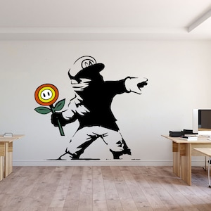 May include: A black and white wall decal featuring a silhouette of a figure wearing a cap with an M logo, throwing a colourful fire flower with orange, yellow, and green petals. The design is applied to a plain white wall in an office space.