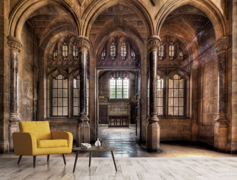 May include: An interior shot of a historic building with stone walls, arched ceilings, and large windows. A yellow armchair and a small table with a vase are in the foreground. The room has a classic, elegant design.