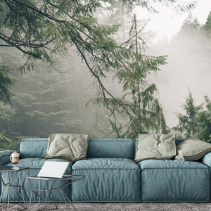 Pode incluir: Um sof&aacute; azul com almofadas cinzas fica em frente a uma cena de floresta nebulosa. O sof&aacute; &eacute; feito de um tecido macio e texturizado e tem um design moderno.