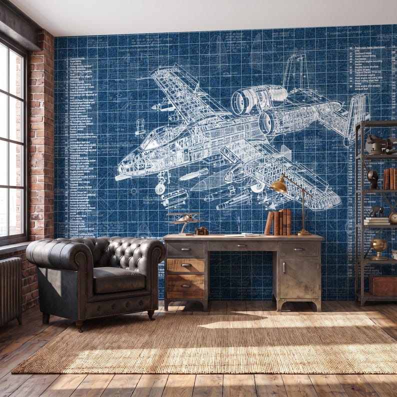 May include: A wall mural featuring a detailed white technical blueprint of a military aircraft on a dark blue grid background, complete with technical annotations and labels, covering the entire wall behind a desk and a tufted leather armchair.