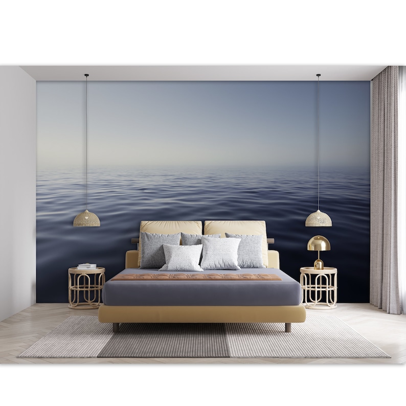 May include: A bedroom interior with a bed, two end tables, and two hanging lamps. The wall behind the bed features a mural of a calm, blue ocean with a hazy horizon.