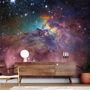 Puede incluir: Una c&oacute;moda de madera marr&oacute;n oscuro con tres cajones y una l&aacute;mpara blanca en el lado izquierdo. La c&oacute;moda est&aacute; delante de una pared con un papel tapiz con una escena de nebulosa gal&aacute;ctica espacial colorida.