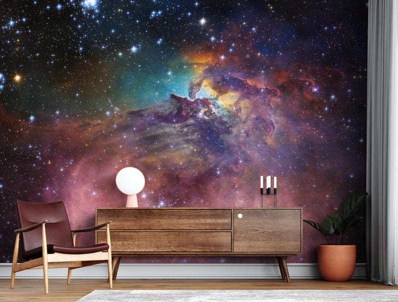 Puede incluir: Una c&oacute;moda de madera marr&oacute;n oscuro con tres cajones y una l&aacute;mpara blanca en el lado izquierdo. La c&oacute;moda est&aacute; delante de una pared con un papel tapiz con una escena de nebulosa gal&aacute;ctica espacial colorida.