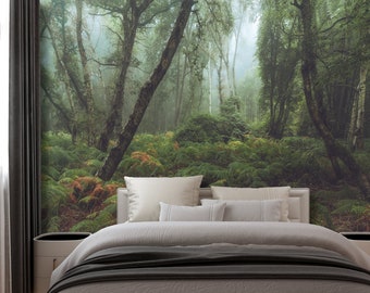 Pode incluir: Um quarto com um grande mural de parede que representa uma cena de floresta nebulosa. O mural apresenta árvores altas com folhas verdes e um leve efeito de nevoeiro. O quarto tem uma cama branca com um cobertor cinza e almofadas brancas.