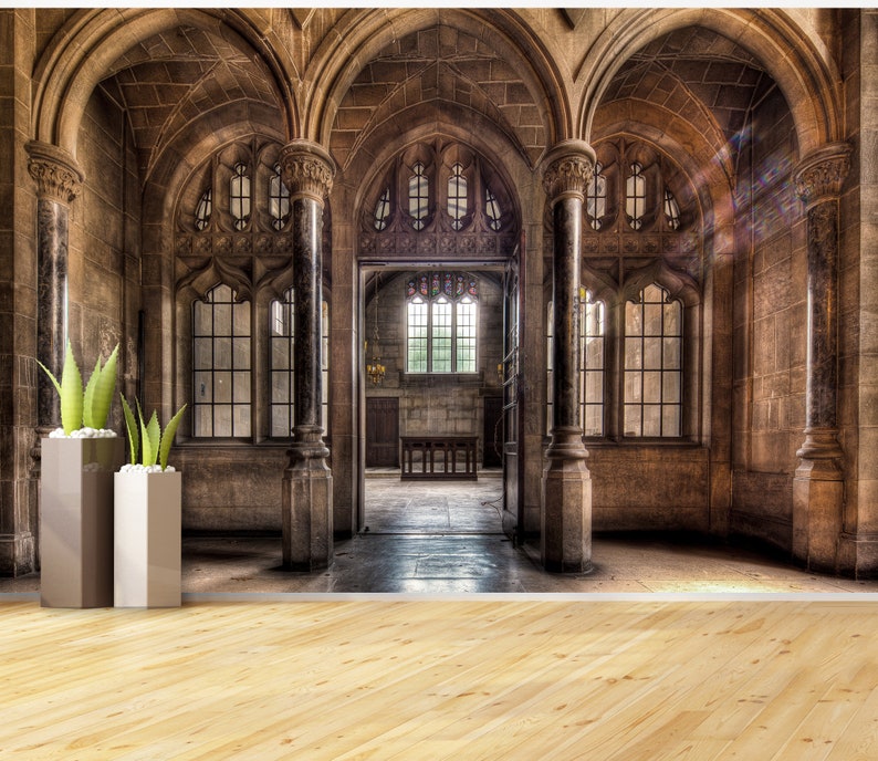 May include: An interior shot of a grand, stone-walled hall with arched ceilings and large windows. Two tall, modern planters with green plants stand in the foreground. The hall features ornate architectural details and a wooden floor.