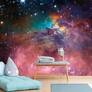 Puede incluir: Un fut&oacute;n azul con dos almohadas frente a un mural de pared que representa una nebulosa colorida con estrellas. Una mesa de madera con una manta gris y una l&aacute;mpara se encuentra frente al fut&oacute;n.