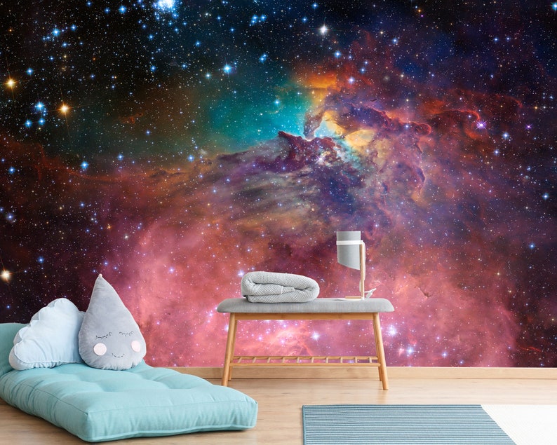 Puede incluir: Un fut&oacute;n azul con dos almohadas frente a un mural de pared que representa una nebulosa colorida con estrellas. Una mesa de madera con una manta gris y una l&aacute;mpara se encuentra frente al fut&oacute;n.