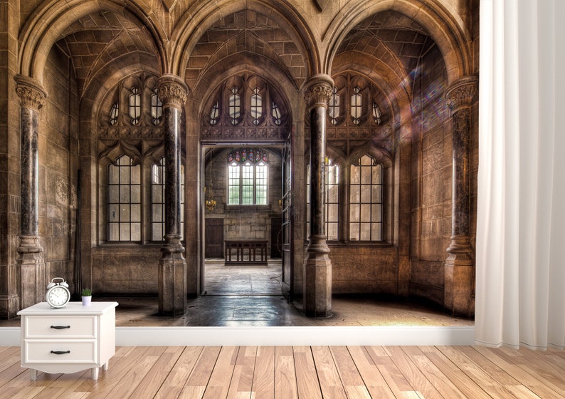 May include: An interior scene of a stone cathedral with arched doorways and large windows. The walls are a warm brown color, and the floor is made of wood. A small white nightstand with a clock and a plant sits in the foreground.