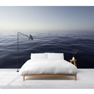 May include: A white bed with a white duvet and two white pillows sits in front of a wall mural depicting a calm, blue ocean.