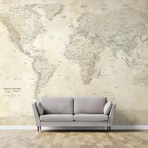 Peut inclure: Une grande carte du monde de style vintage aux tons neutres recouvre un mur. La carte est détaillée avec les noms et les frontières des pays. Un canapé gris est placé devant le mur, et le sol est en bois.