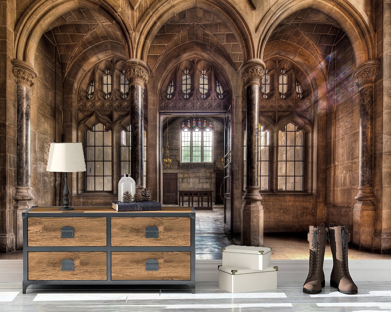 May include: An interior scene featuring a wooden dresser with four drawers, a black lamp, and a pair of brown boots. The room has arched doorways, large windows, and stone walls. Two white boxes are on the floor.