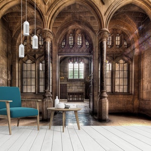 May include: An interior shot of a grand, stone-walled room with arched ceilings and large windows. A teal armchair and a small wooden table with books and vases are in the foreground. Overhead, three white pendant lights hang from the ceiling.