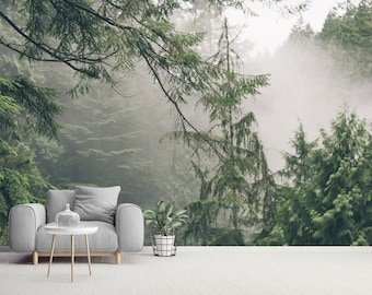 May include: A gray armchair with a small table in front of it. The armchair is in a room with a large window that looks out onto a foggy forest. The forest is made up of tall, green trees.