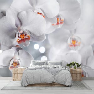May include: A bedroom scene featuring a large, white orchid floral mural as a backdrop. The bed has a gray comforter and pillows, with wooden nightstands on either side. The orchids have orange and red centers.