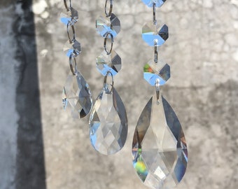 May include: Three strands of crystal teardrop-shaped beads hang from silver metal rings. The beads are clear and have a faceted design.