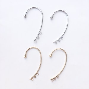 May include: Four ear cuff earring findings, two silver and two gold. Each ear cuff has a small ball at the top and three jump rings hanging from the bottom.