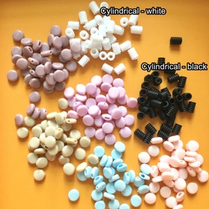 Könnte beinhalten: Sortiment an bunten Silikon-Ohrstöpsel-Spitzen in verschiedenen Farben, darunter rosa, beige, hellblau und lila. Die Ohrstöpsel-Spitzen sind in Gruppen auf einer gelben Oberfläche angeordnet. Der Text "Cylindrical - white" und "Cylindrical - black" ist im Bild sichtbar.