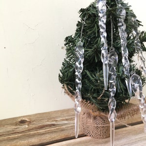 Puede incluir: Un pequeño árbol de Navidad artificial decorado con adornos de carámbanos de plástico transparente. El árbol está en una maceta de arpillera.