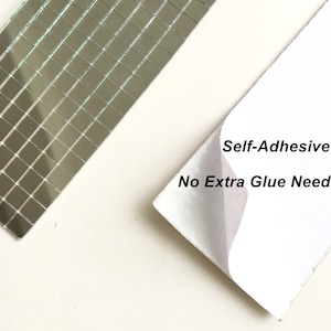 May include: A sheet of self-adhesive mirror tiles. The tiles are small and square, and they are arranged in a grid pattern. The sheet is white and has the text "Self-Adhesive No Extra Glue Need" printed on it.
