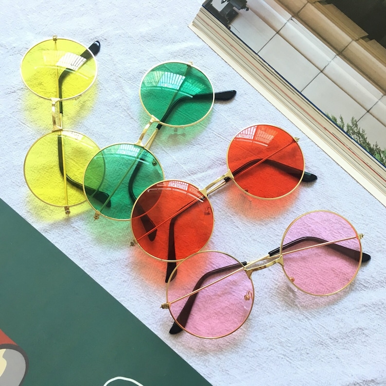 May include: Six pairs of round, colorful sunglasses with gold frames. The lenses are yellow, green, red, pink, and two more pairs of green.
