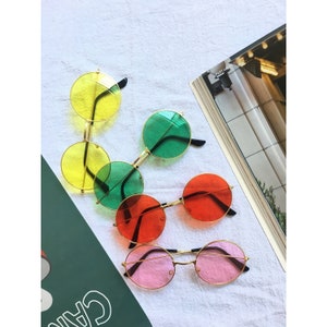 May include: Five pairs of round sunglasses with different colored lenses. The lenses are yellow, green, red, and pink.