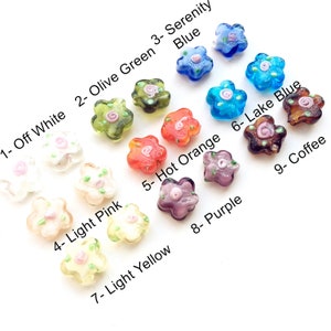 May include: Nine glass flower-shaped beads in various colours, including off white, olive green, serenity blue, light pink, hot orange, lake blue, light yellow, purple, and coffee. Each bead has a small pink flower design in the centre.