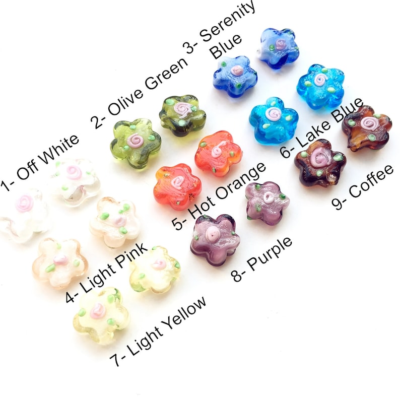 May include: Nine glass flower-shaped beads in various colours, including off white, olive green, serenity blue, light pink, hot orange, lake blue, light yellow, purple, and coffee. Each bead has a small pink flower design in the centre.