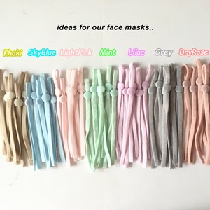 Könnte beinhalten: Eine Auswahl an Farben für Gesichtsmasken-Verlängerungen mit verstellbaren Stoppern. Die Farben sind Khaki, Himmelblau, Hellrosa, Mint, Lila, Grau und Trockenrose.