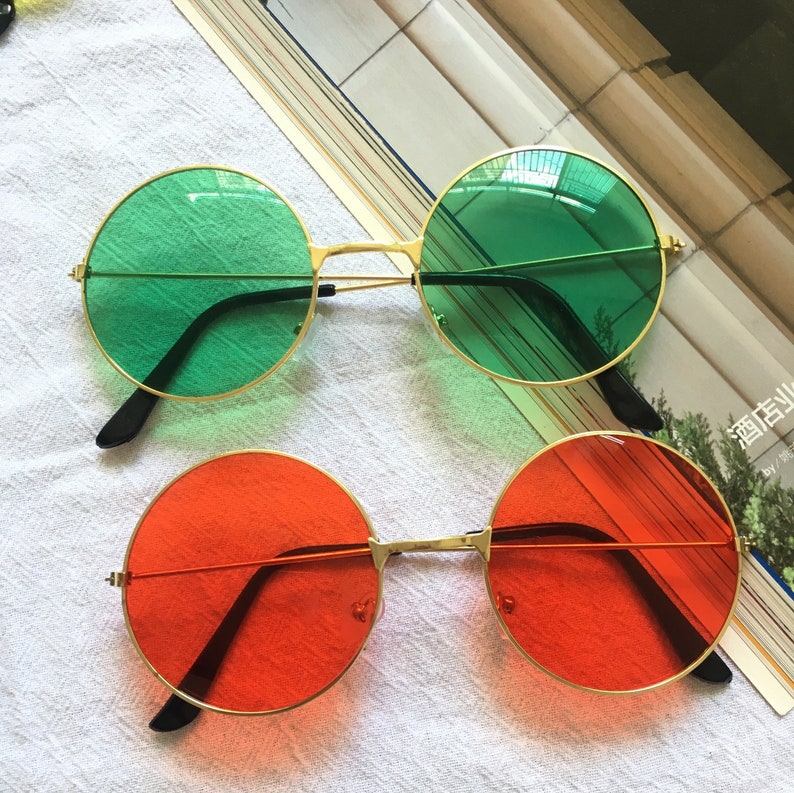May include: Two pairs of round sunglasses with gold frames. One pair has green lenses and the other pair has orange lenses.
