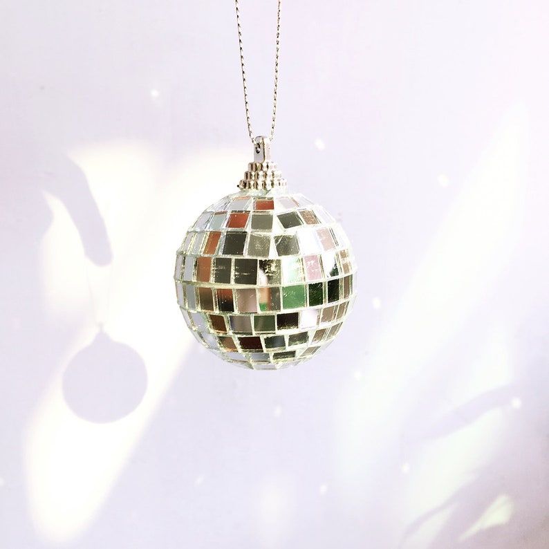 May include: A silver disco ball ornament hanging from a silver chain. The ornament is made of many small mirrored squares.