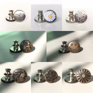 May include: Assortment of 10 metal snap buttons with various designs, including a daisy, a rose, a smiley face with the word "LOVE", a floral pattern, and a geometric pattern. The buttons are silver and gold in colour.