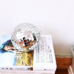 May include: A silver disco ball sits on top of a stack of books. The books are in Chinese and English. The text on the books reads "Out of the Wilderness" and "Lady Chatterley's Lover".