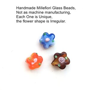 May include: Three handmade millefiori glass beads in the shape of flowers. The beads are blue, orange, and brown with white and green accents. Each bead has a unique, irregular shape.
