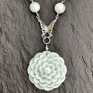 May include: A jade necklace with a carved flower pendant and a silver butterfly clasp. The necklace is made of round jade beads and is strung on a silver chain.