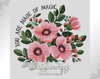 May include: A cross stitch pattern featuring a floral arrangement of pink flowers with dark centres and green leaves. The text "YOU ARE MADE OF MAGIC" is arched over the flowers in black, with "You are made of magic" below in white.