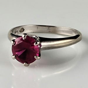 May include: A 10K gold ring with a prong-set ruby gemstone. The ruby is a deep red color and has a round shape.
