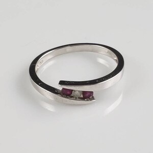 May include: A silver ring with a twisted band and three small gemstones. The gemstones are two red rubies and one white diamond.