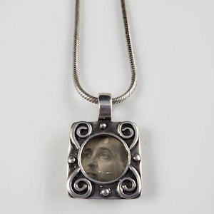 May include: A silver chain necklace with a silver pendant featuring a framed black and white photograph of a person's face.