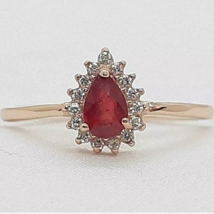 May include: A pear-shaped ruby ring set in a rose gold band with a halo of small diamonds.
