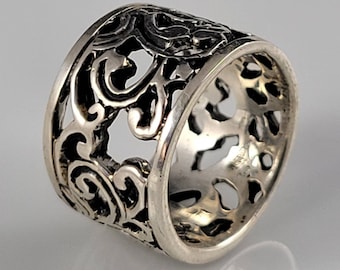 Puede incluir: Anillo de plata con un diseño calado intrincado. El anillo es ancho y tiene un patrón de filigrana.